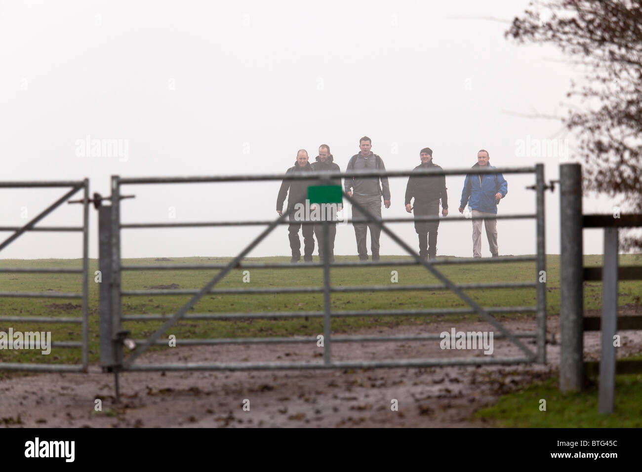 group of walkers approching metal countryside gate from the mist Stock Photo