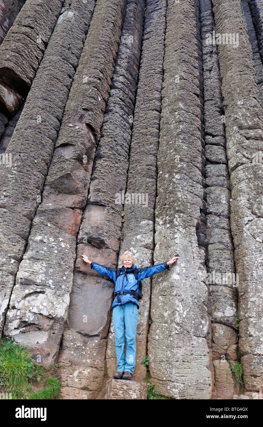 Mature woman standing at the base of the 'Organ' near to the Giant's Causeway. County Antrim, Ulster, Northern Ireland, UK. Stock Photo