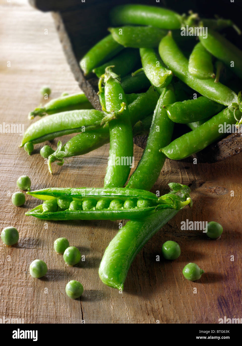 Food still life of fresh picked garden peas and pea in pods  on a rustic table in a kitchen being prepared Stock Photo