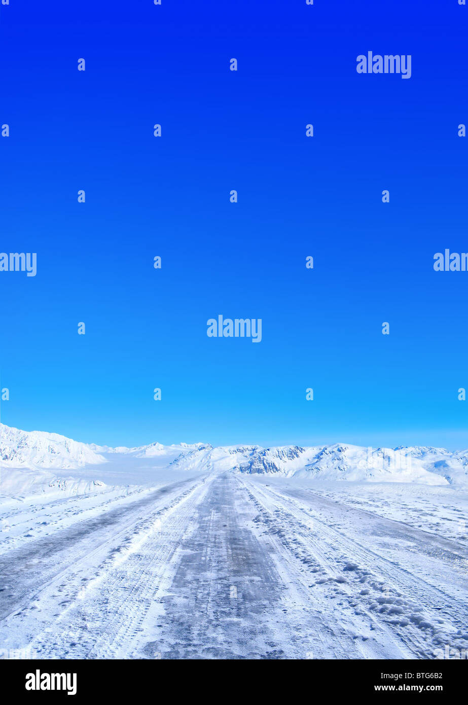 Snow covered road in winter with mountains in the distance Stock Photo