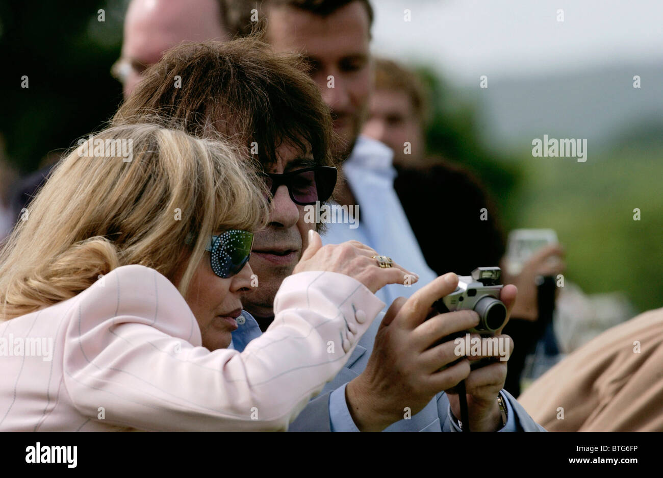 Rolling Stones rock star Bill Wyman with his digital camera and actress Britt Ekland watching polo match, Surrey Stock Photo