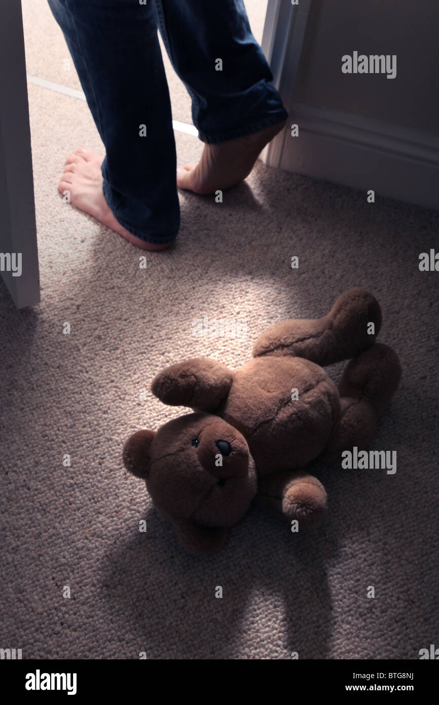 Child's teddy bear lying on the floor of a carpeted room as a man's feet step in through an open door Stock Photo