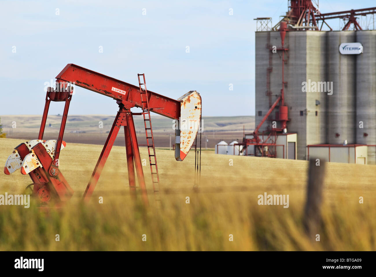 Prairie wheat field, oil well pump jack and inland grain terminal.  Gull Lake, Saskatchewan, Canada. Stock Photo