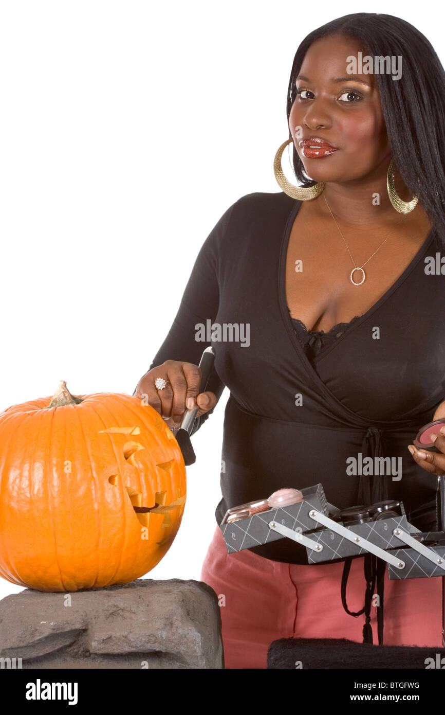 Beautiful African-American make up artist applying makeup on Halloween carved pumpkin (Jack O' Lantern) Stock Photo