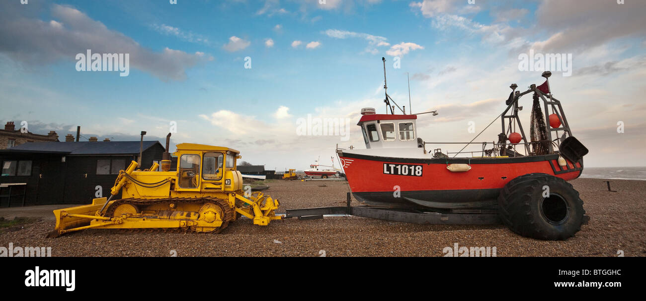 Yellow caterpillar tractor with a red fishing boat on a trailer, parked