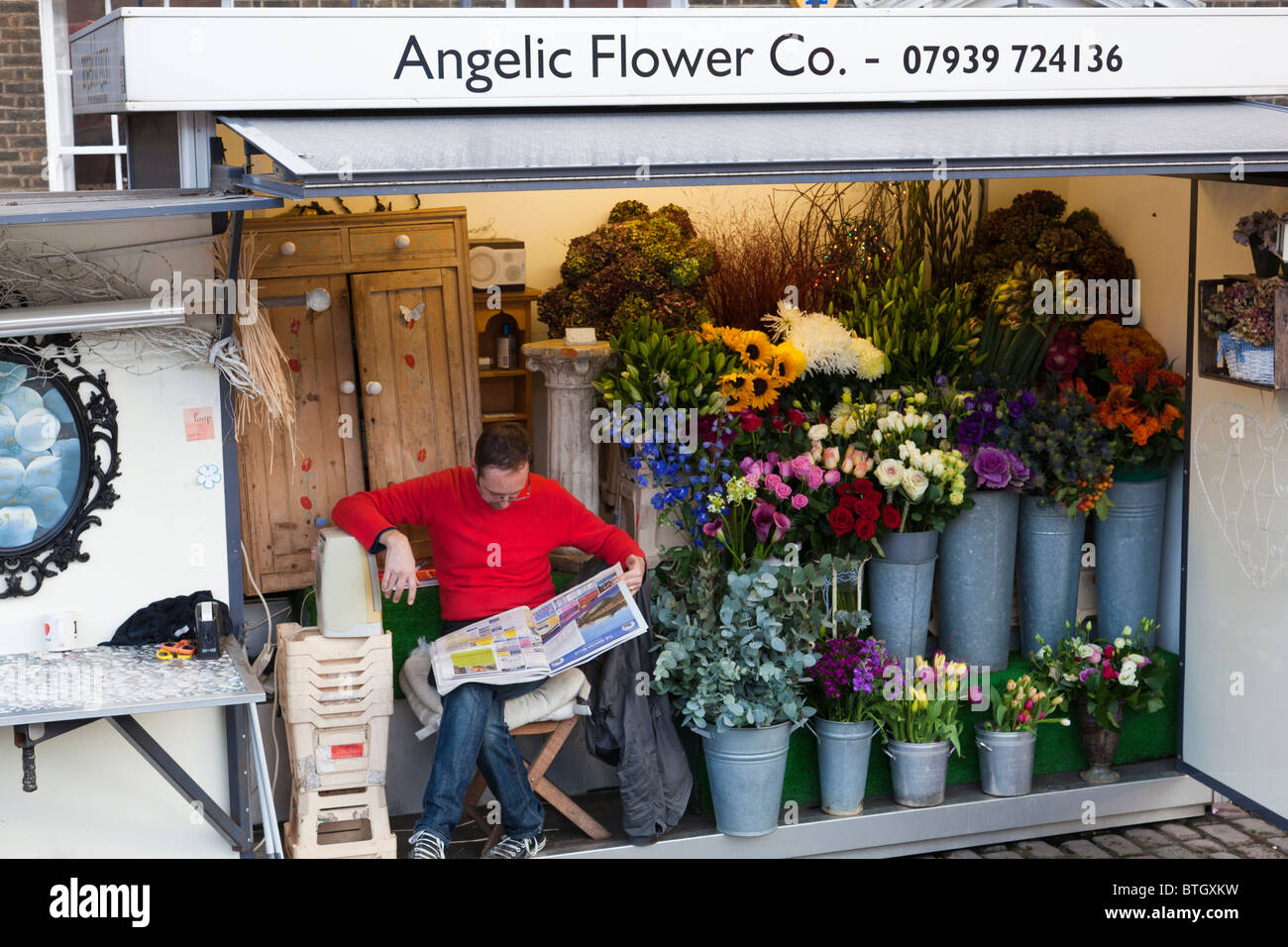 A flower seller reads the paper alongside his display of flowers, London, England Stock Photo
