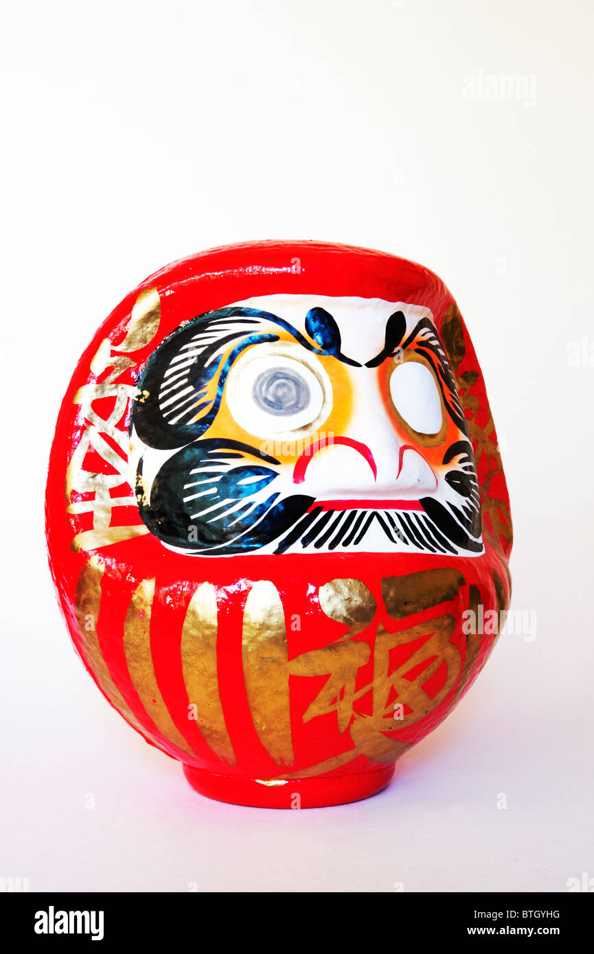 A red and white daruma head, with one eye painted, on a white background. Stock Photo