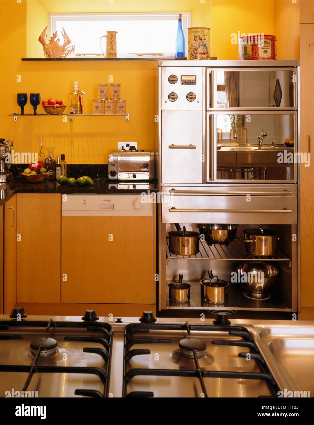 Gas hob in island unit in yellow kitchen with shelves below stainless