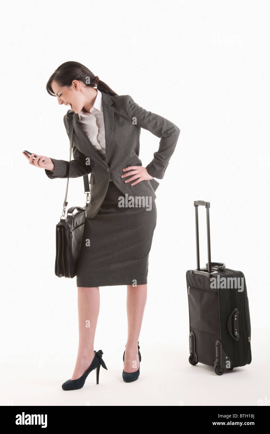 Young woman in suit with wheeled suitcase screaming at phone Stock Photo