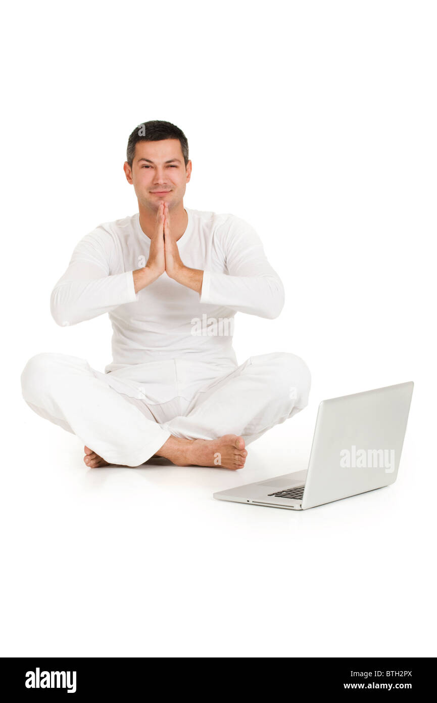 man dressed in white sitting on the floor practicing yoga with laptop ...
