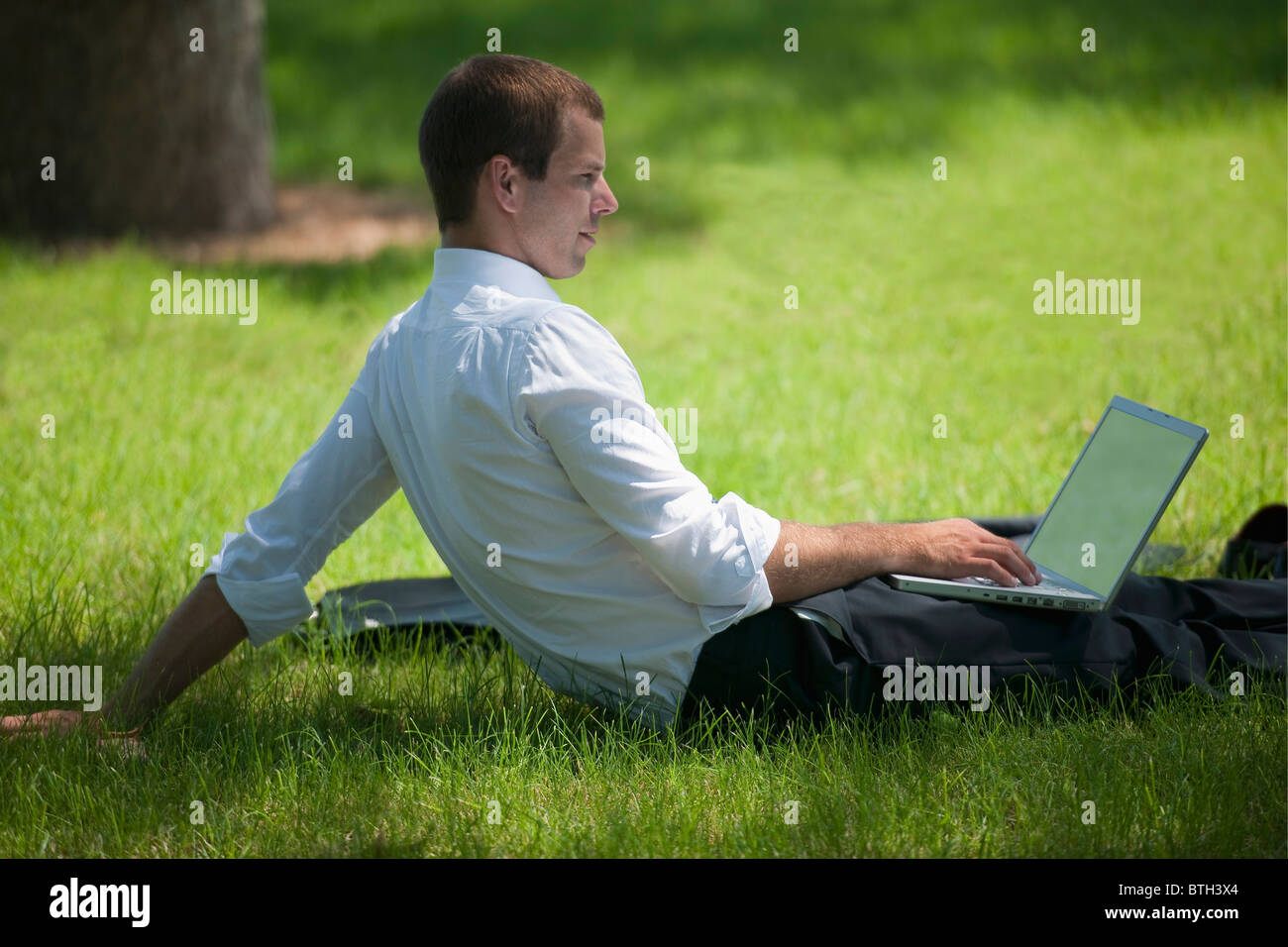 Man sitting in grass with laptop Stock Photo - Alamy
