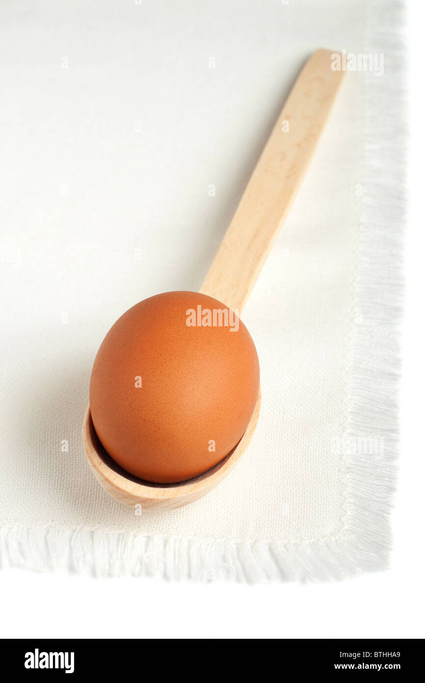 Brown egg in a wooden spoon on a white napkin Stock Photo