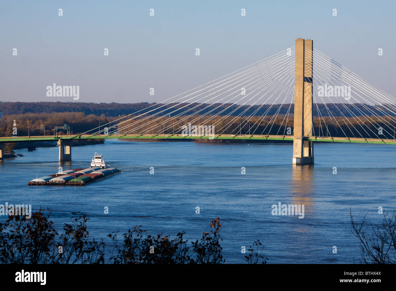 A barge heads down the Mississippi River, under the US Highway 34 suspension bridge at Burlington, Iowa. Stock Photo