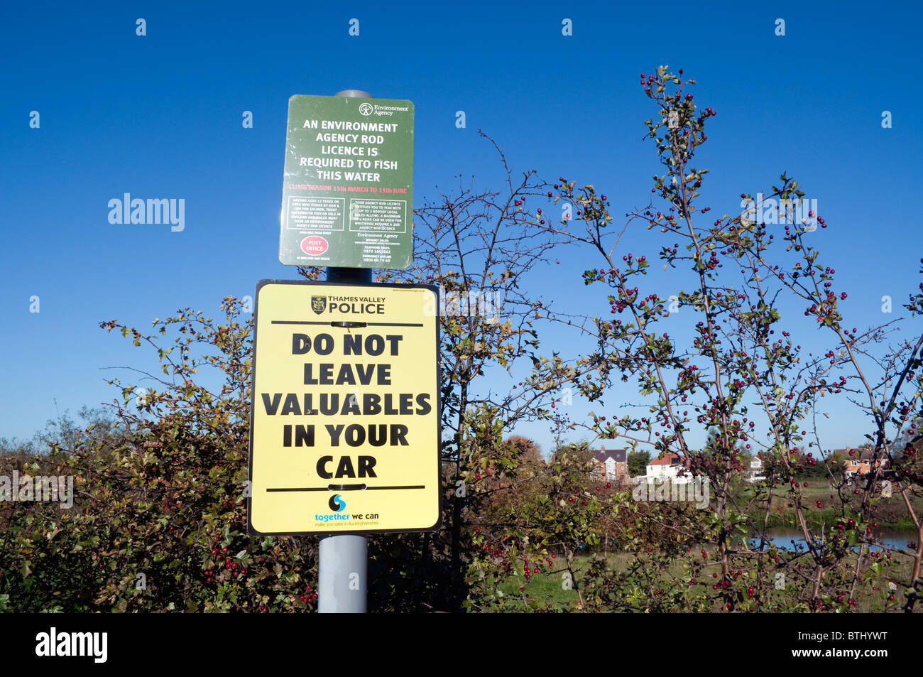 Two public signs and notices, a security warning sign and fishing notice on a metal post against a clear blue sky Stock Photo