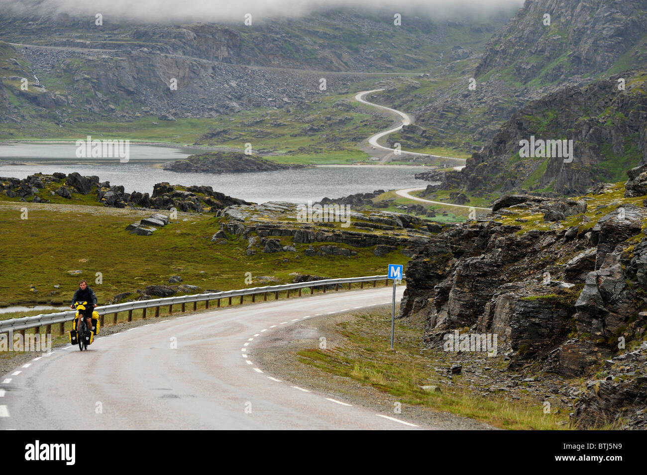 Cyclist on a curvy road in barren landscape. The road to Havøysund, Finnmark, North Norway Stock Photo