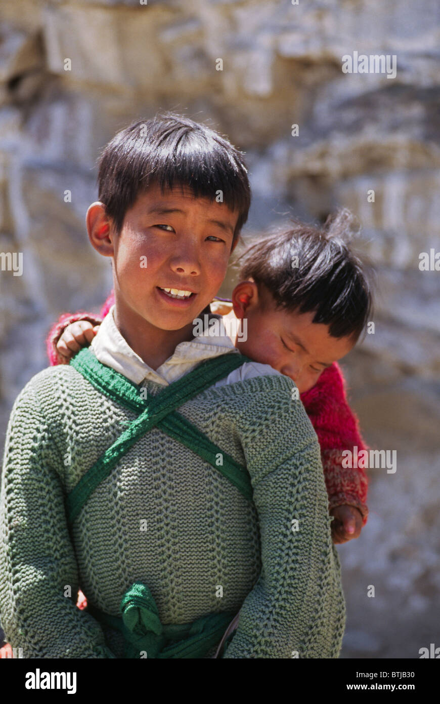 A TIBETAN BOY carries his little brother in a small village - CENTRAL, TIBET, CHINA Stock Photo