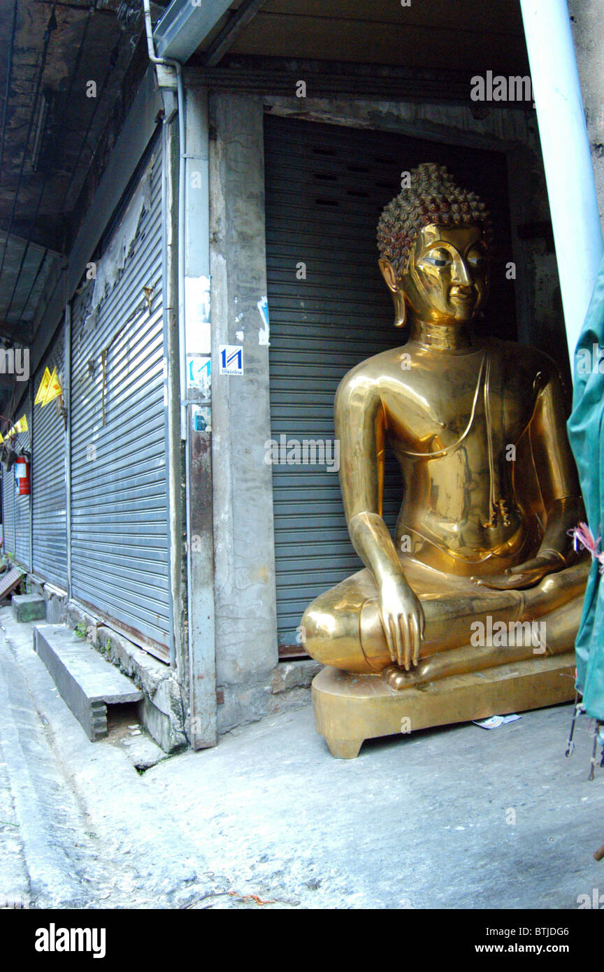 Buddha in alleyway outside a workshop in Bangkok. Stock Photo