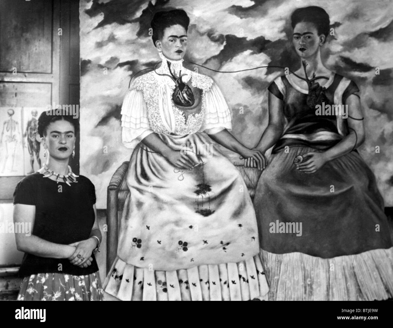 Frida Kahlo shown with her painting Me Twice. The painting shows Kahlo as a 19th century lady linked by an artery to herself dre Stock Photo