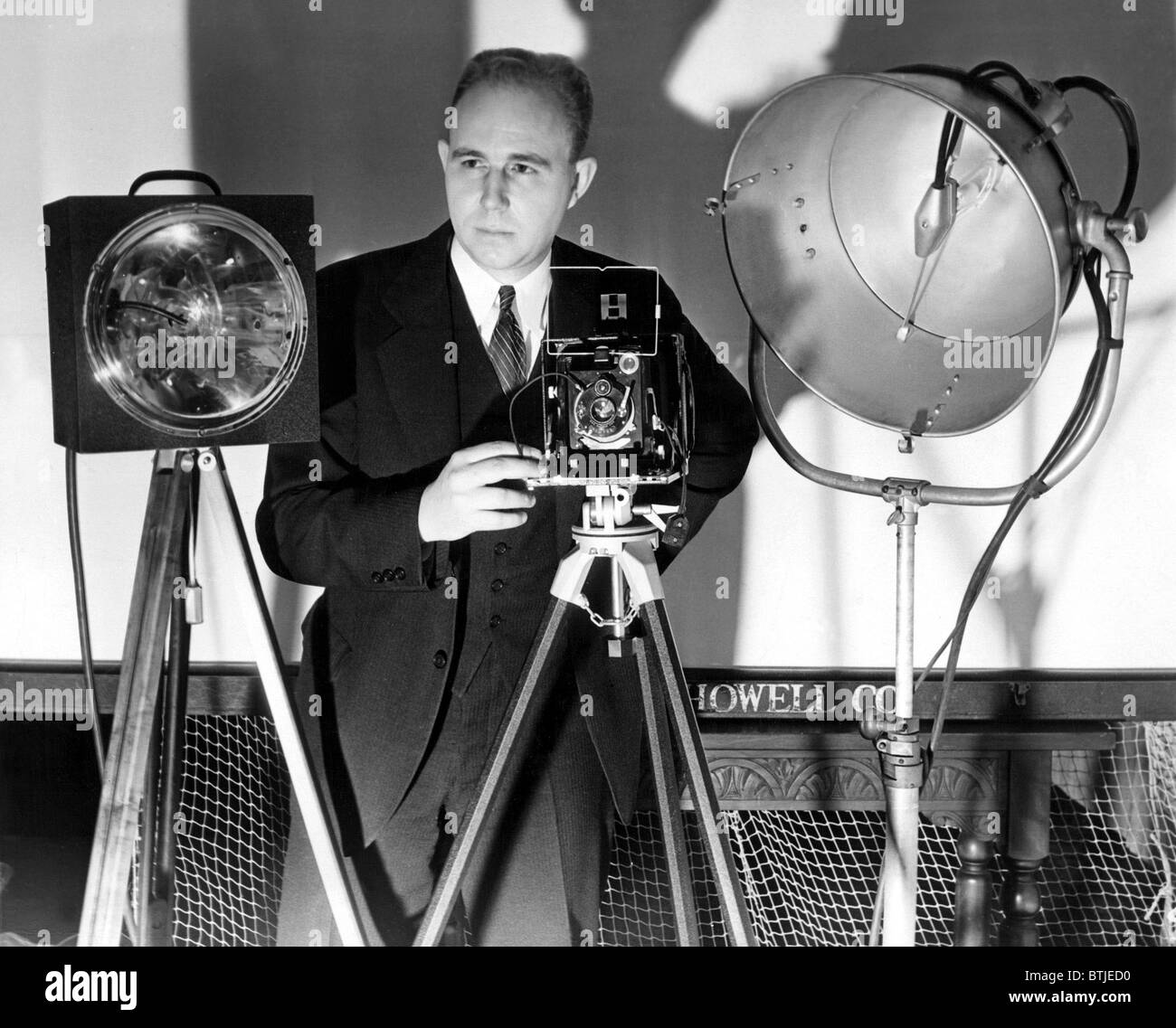 Dr. Harold Edgarton, of M.I.T., stands behind his camera that boasts ultra-speed photography, with pictures being taken at 1/100 Stock Photo