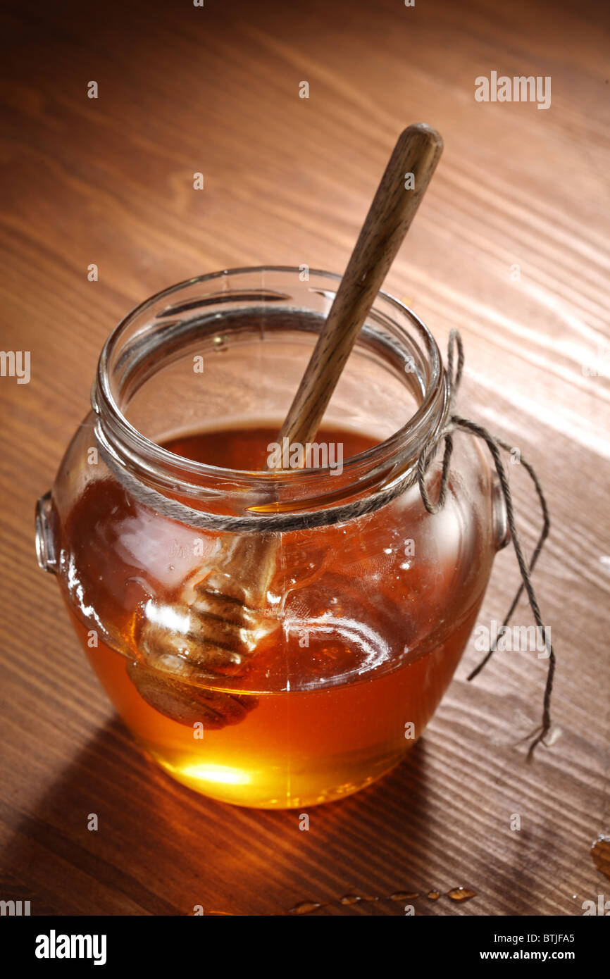 Pot of honey and wooden stick in it. Objects are on wooden table. Stock Photo