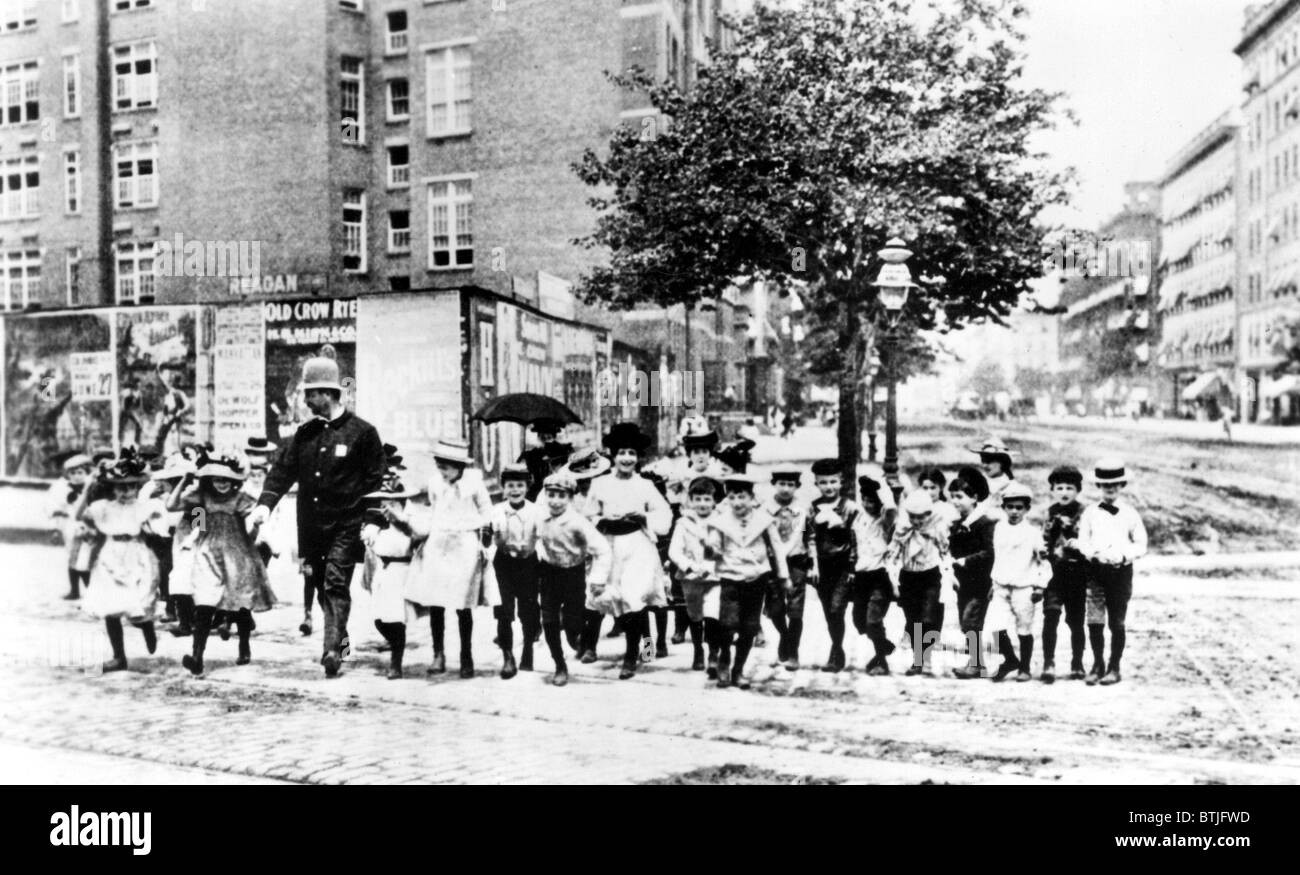 Policeman helping a group of neighborhood children cross the street in N.Y.C. in 1910. Stock Photo
