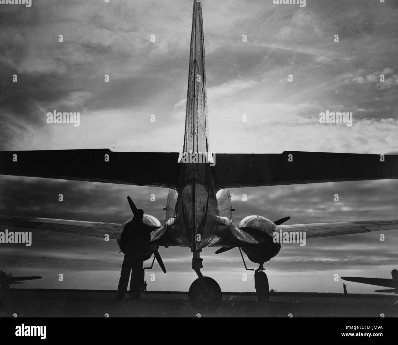World War II, soldier beside WWII airplane at sunrise, circa early 1940s. Stock Photo