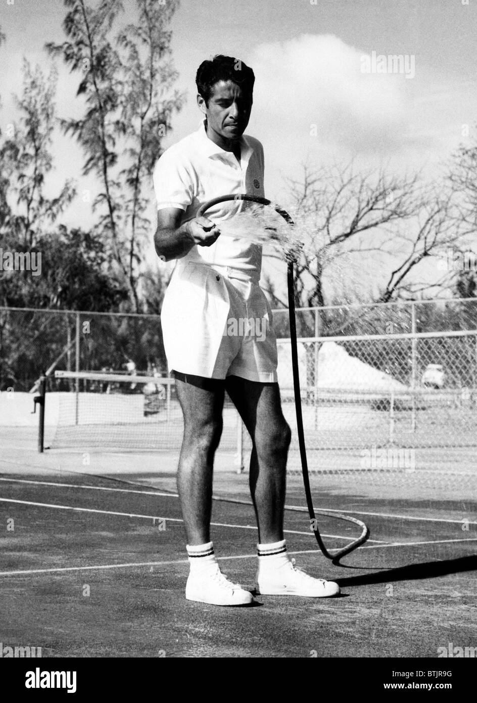 Tennis player Pancho Gonzales hosing off his courts in the Bahamas
