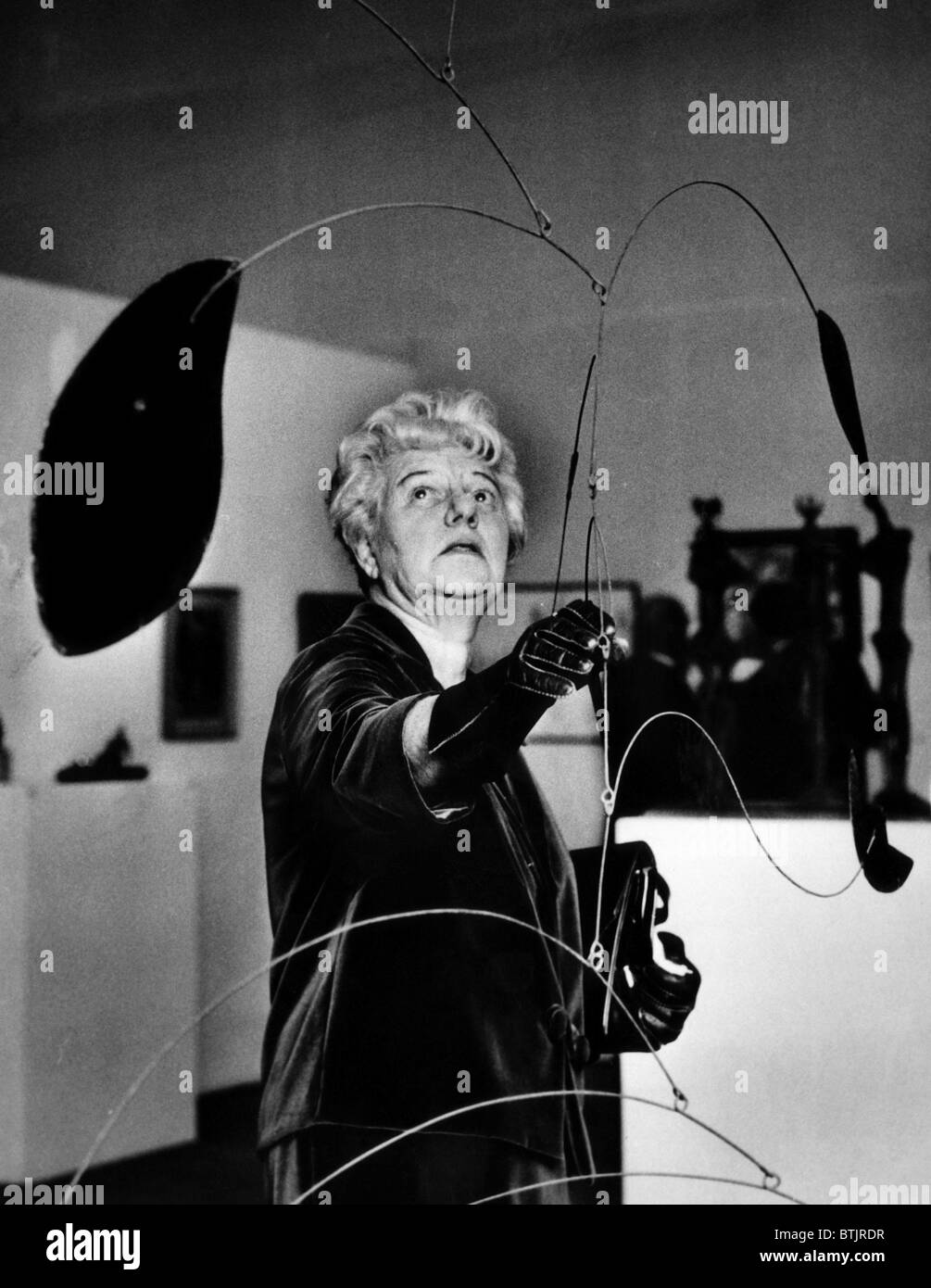 Peggy Guggenheim adjusts Alexander Calder's 'Mobile' at a special exhibit of her famed collection of art at the Tate Gallery, Lo Stock Photo
