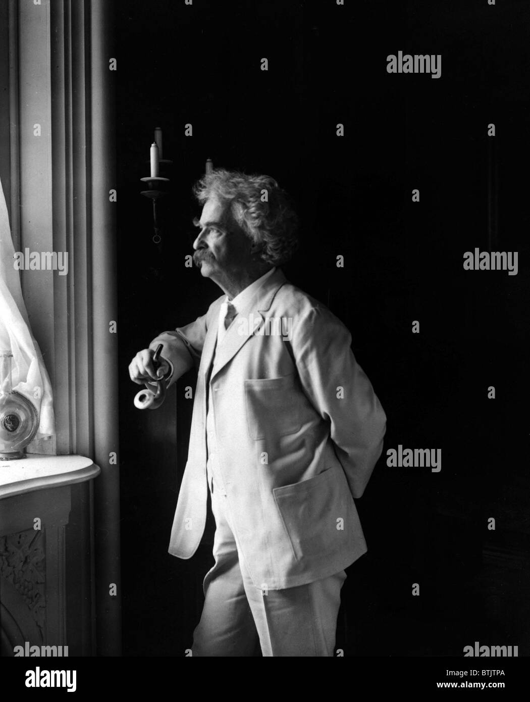 Mark Twain (Samuel L. Clemens, 1835-1910) American humorist standing by window in 1907 portrait. Stock Photo