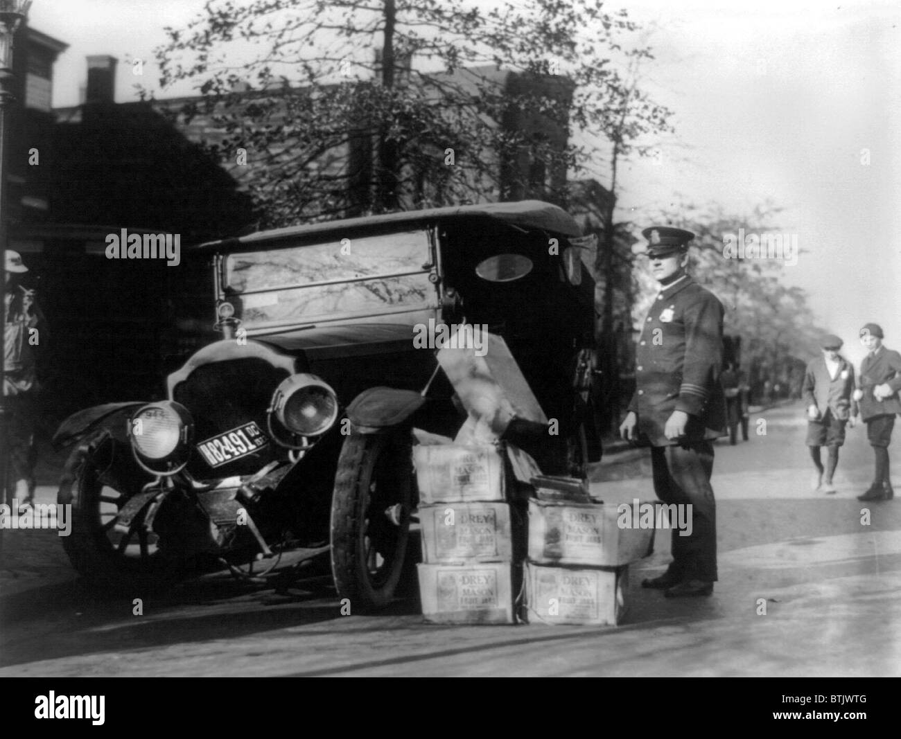 Prohibition, a policeman standing alongside a wrecked car and cases of moonshine, November 16, 1922. Stock Photo