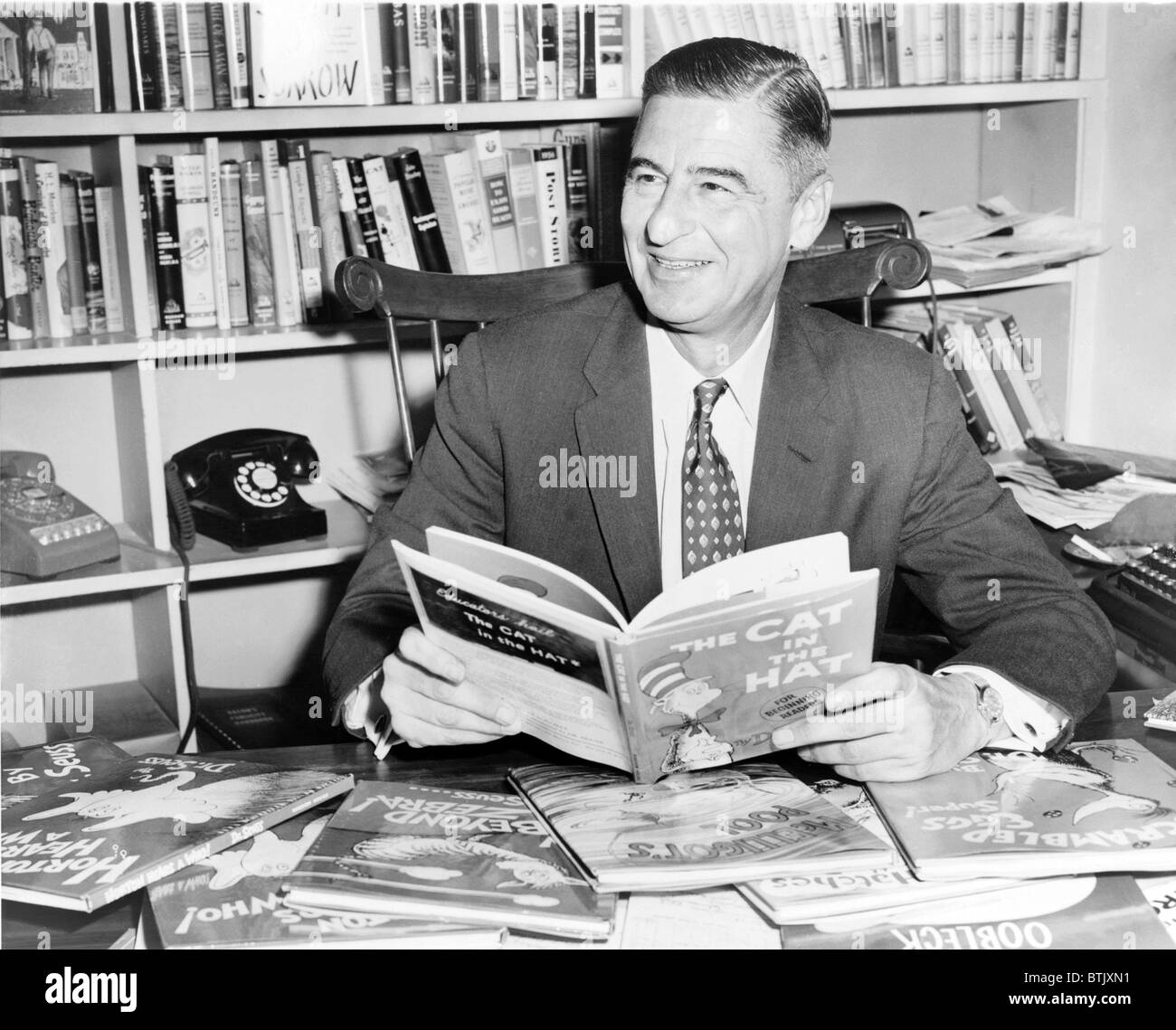 Ted Geisel (Dr. Seuss) (1904-1991) seated at desk covered with his uniquely humorous children's books. 1957. Stock Photo