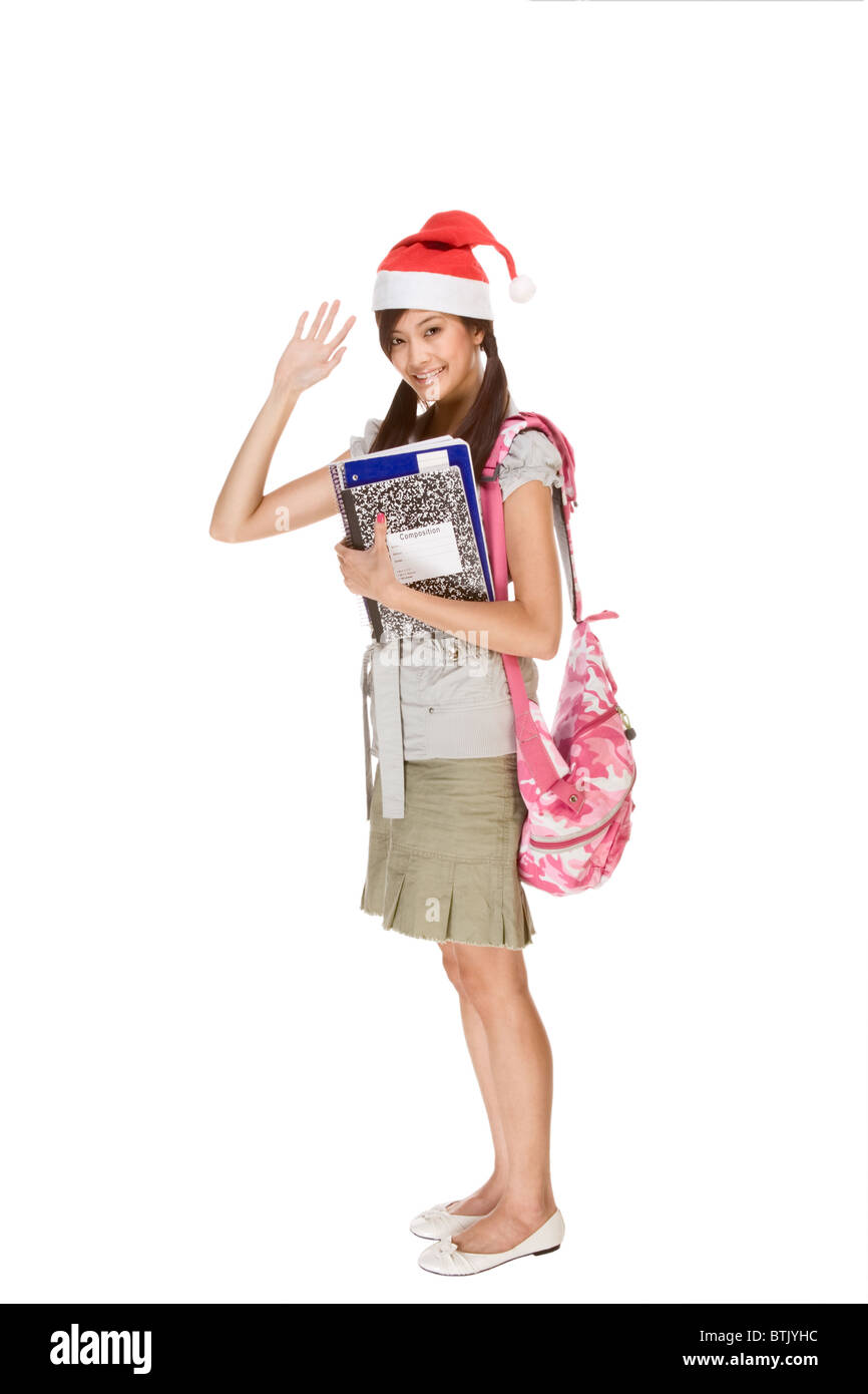 Asian school girl wearing red Santa Claus hat with backpack holding Composition book, notebooks and pen waives her hand greeting Stock Photo