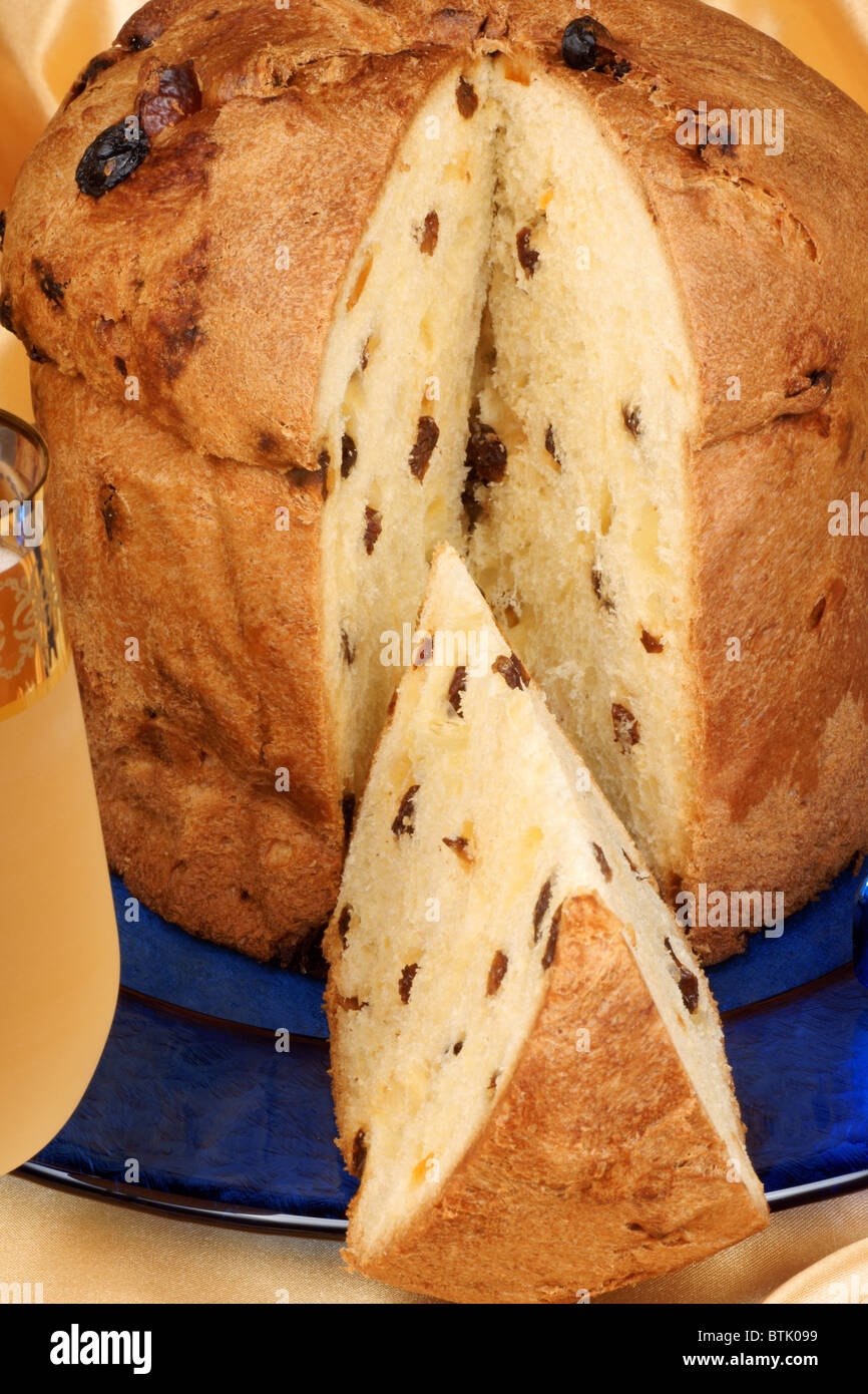 Panettone the italian Christmas fruit cake served on a blue glass plate over a yellow background and a glass of spumante. Stock Photo