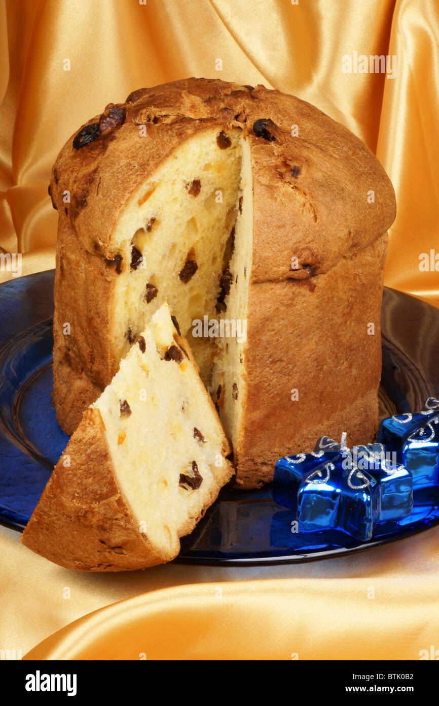 Panettone the italian Christmas fruit cake served on a blue glass plate over a yellow background and two candles. Stock Photo