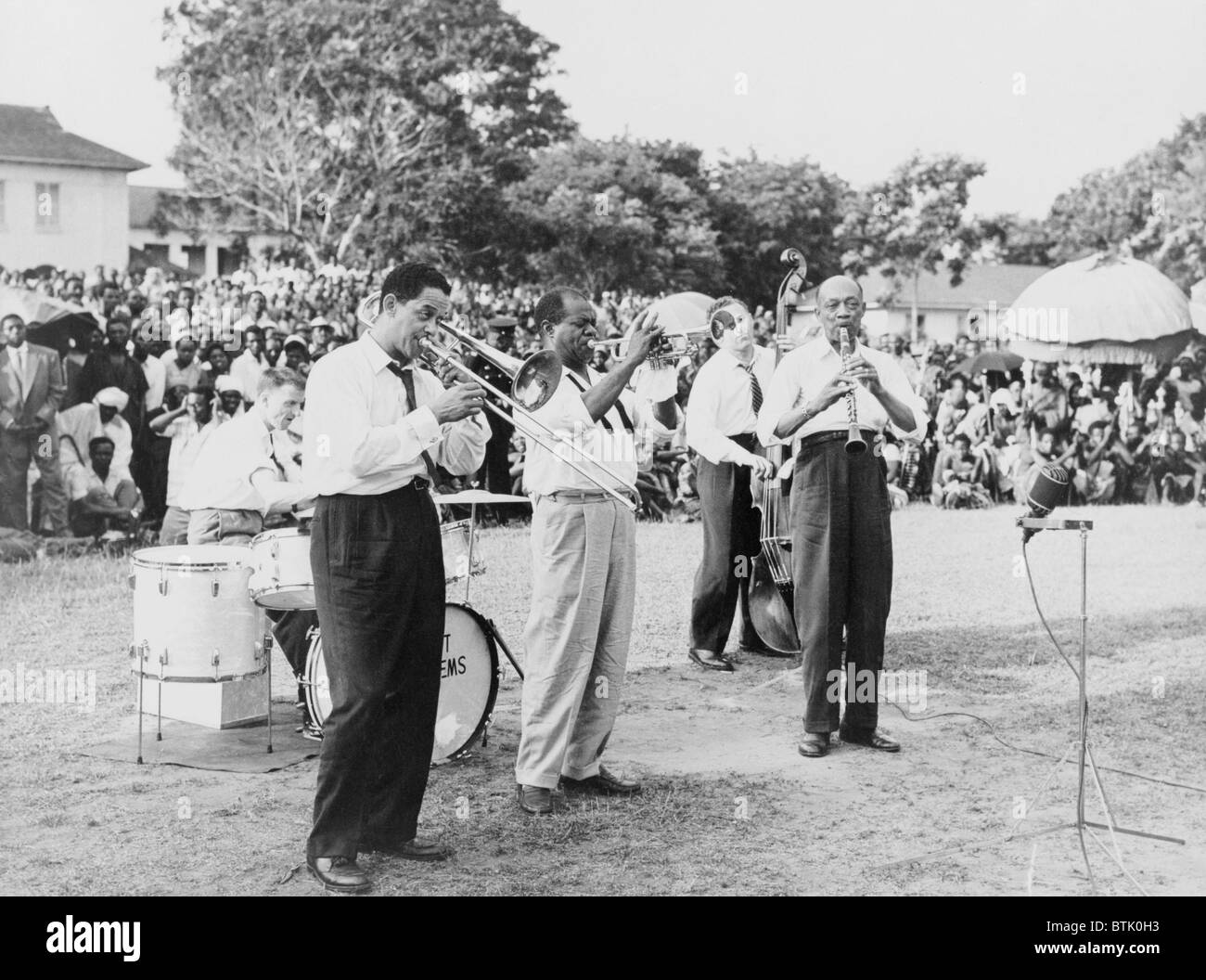 Louis Armstrong (1901-1971), African American Jazz musician, playing trumpet with band at an outdoor gathering in Africa, 1956. Stock Photo