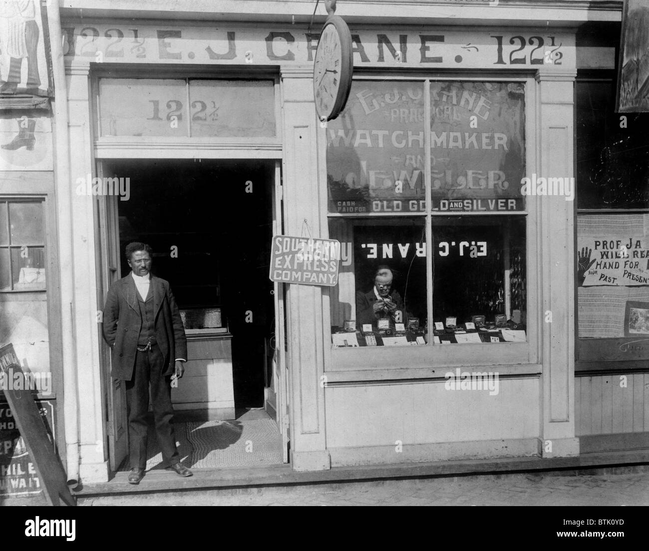 African American watchmaker, original title: 'E.J. Crane, watchmaker and jewelry store with man working in window and man standing in doorway', Richmond, Virginia, photograph, 1899. Stock Photo