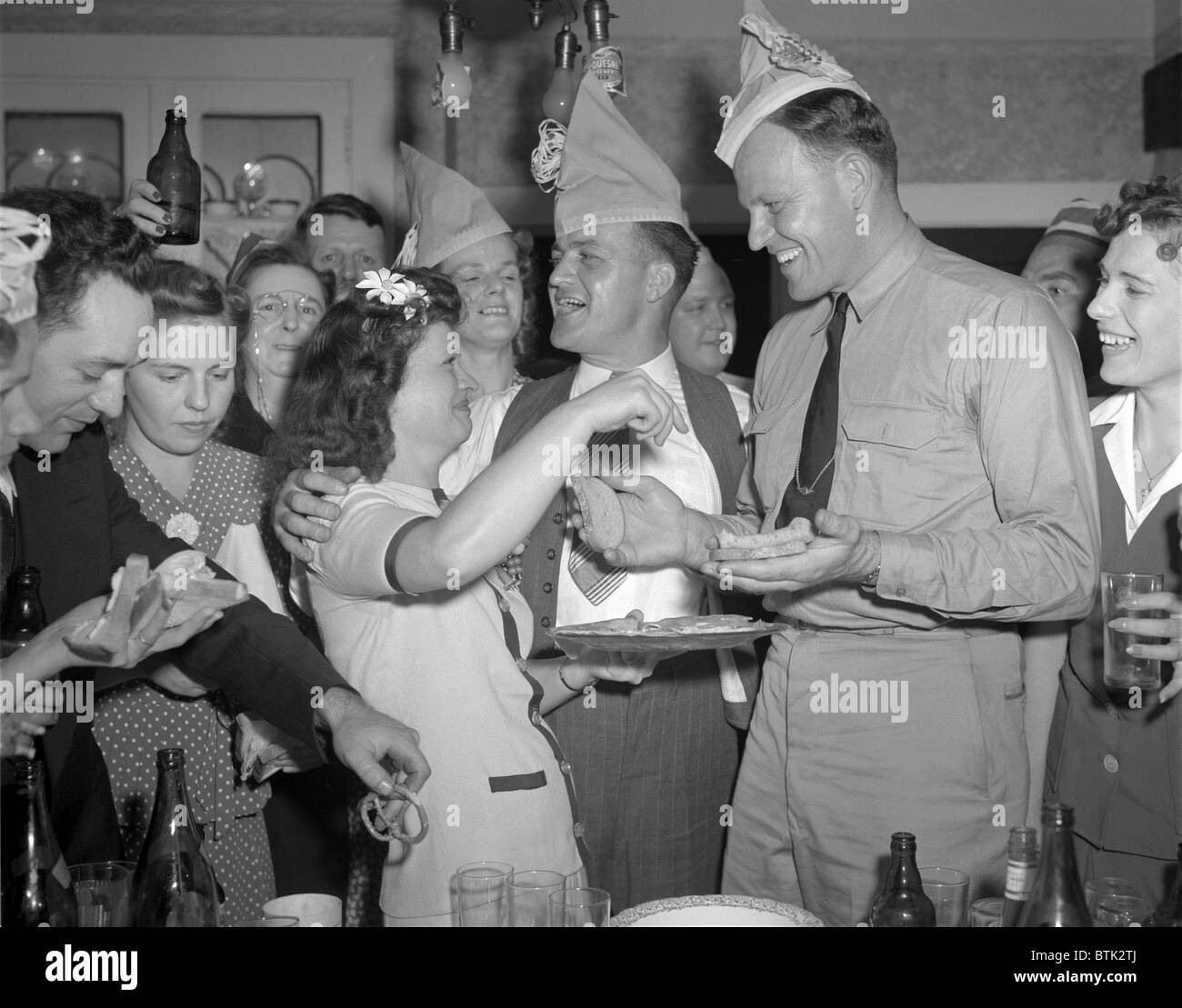 World War II, George Woolslayer (center), soldier and sailor with a party at his home, friends, relatives and fellow workers made up the list of guests, Mrs. Woolslayer (left of center) helps Chief Evans (right), to a sandwich, Pittsburgh, Pennsylvania, photograph by Alfred T. Palmer, August, 1942 Stock Photo