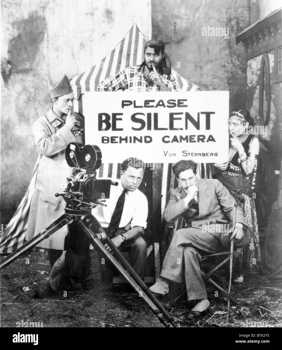 Josef von Sternberg during the shooting of MGM's silent film, EXQUISTE SINNER in 1926. Conrad Nagel (left), Matthew Betz (behind sign) and Renee Adoree pose for a gag shot behind cameraman Maximilian Fabian and von Sternberg. Stock Photo