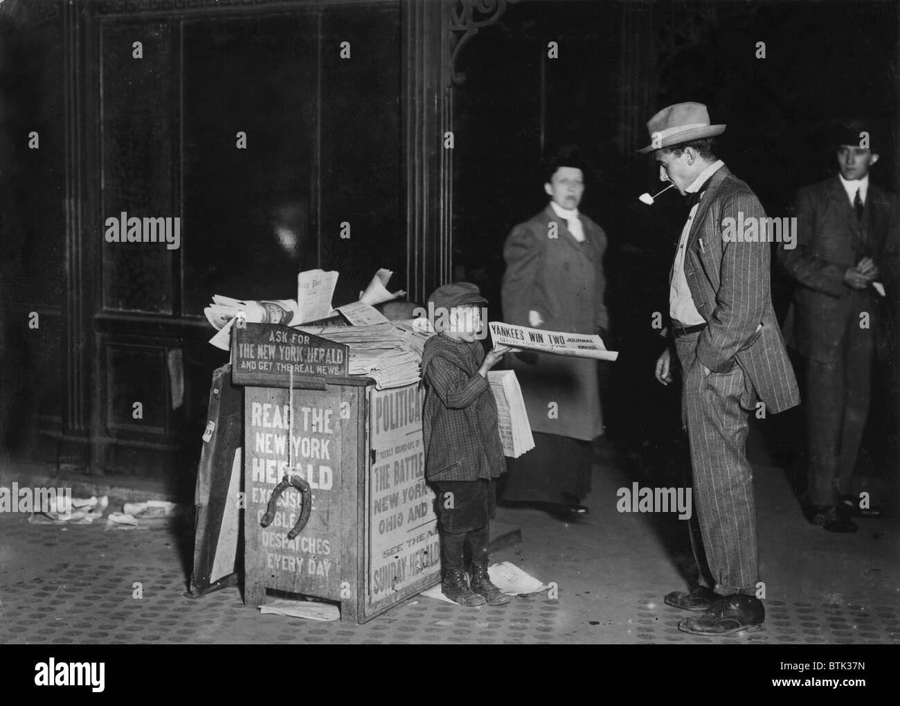 Child labor, Jerald Schaitberger of 416 W. 57th Street, who helps an older boy sell papers until 10 P.M. on Columbus Circle. 7 years old. 9:30 P.M., the newspaper announces the 'Yankees win', New York City, photograph by Lewis Wickes Hine, October 8, 1910 Stock Photo