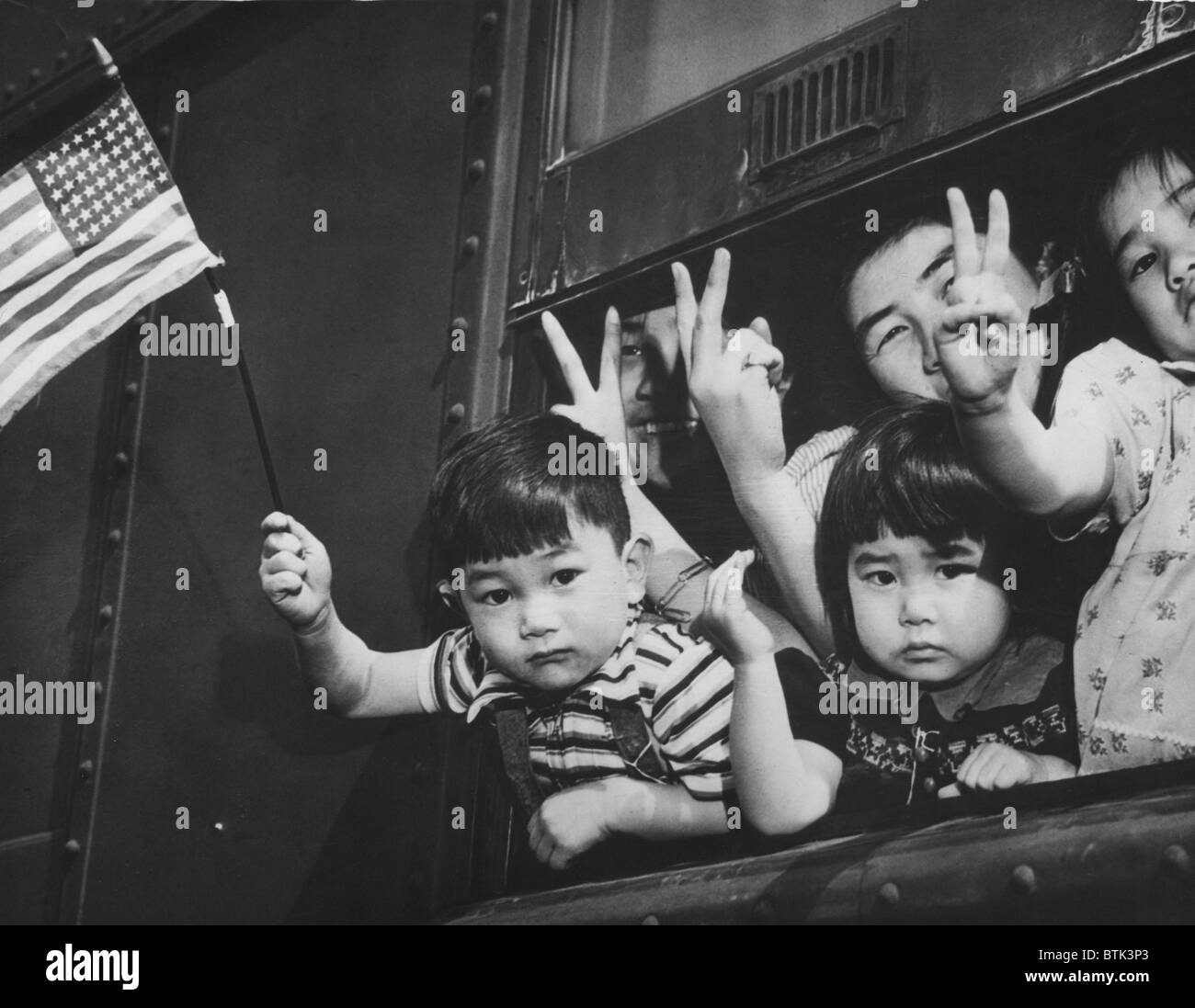 Japanese-American children waving from a train window as it leaves Seattle to take them to an internment camp for the duration of World War II. March 1942. Stock Photo