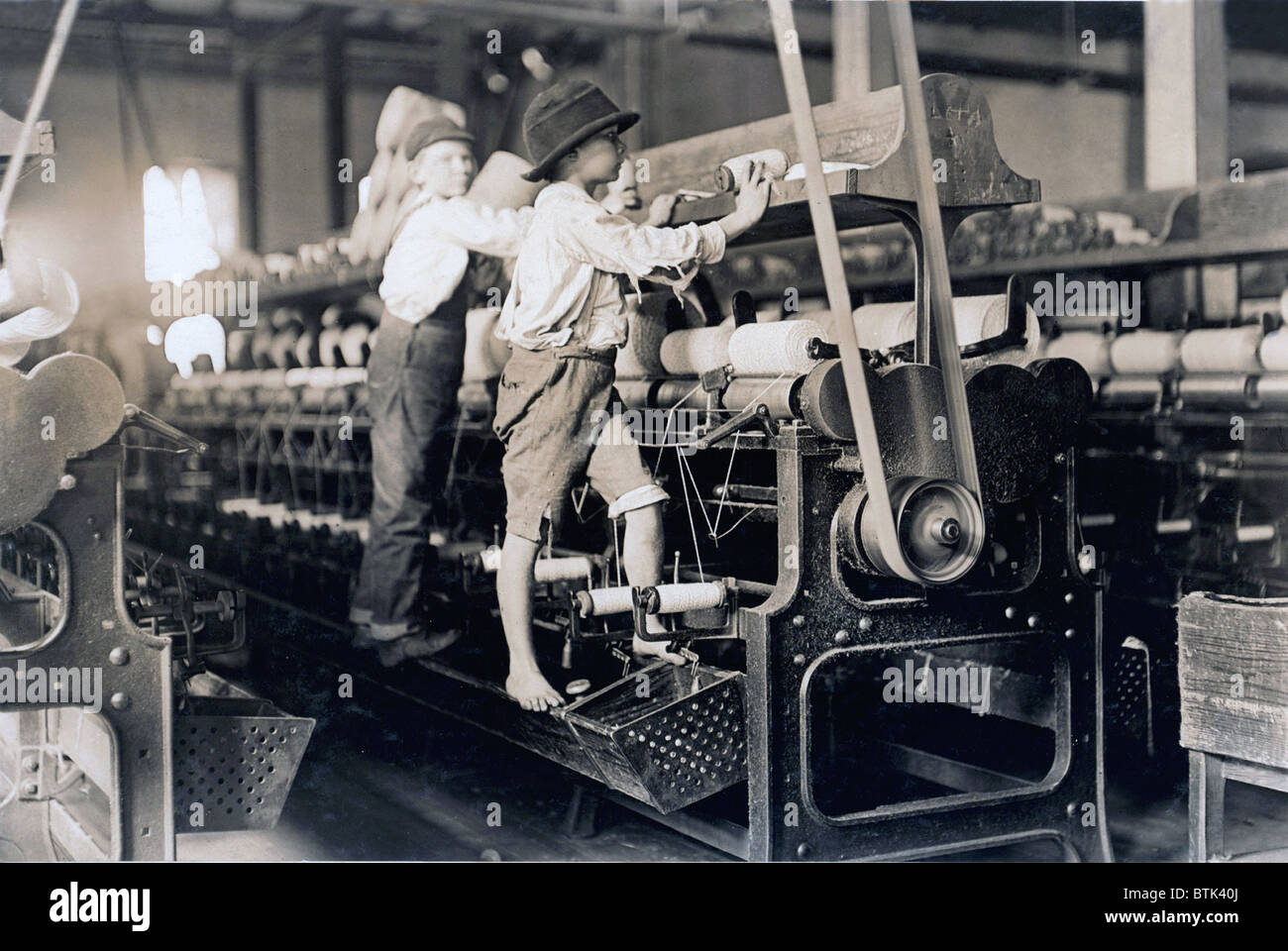 Child laborer portrayed by Lewis Hine in 1909. The barefooted boy in a George cotton mill was so small he had to climb up on the spinning frame to mend the broken threads and put back the empty bobbins. Stock Photo