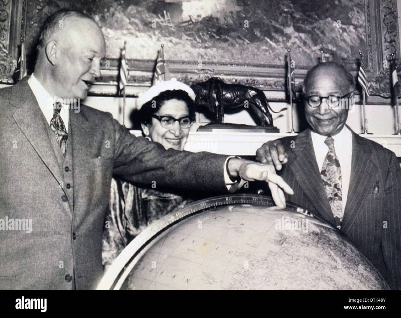 Matthew Henson (1866-1955), African American Arctic explorer, and President Eisenhower discuss the North Pole over a globe at the White House. Mrs. Robert L. Vann, publisher of the African American newspaper, Pittsburgh Courier observes. 1954. Stock Photo