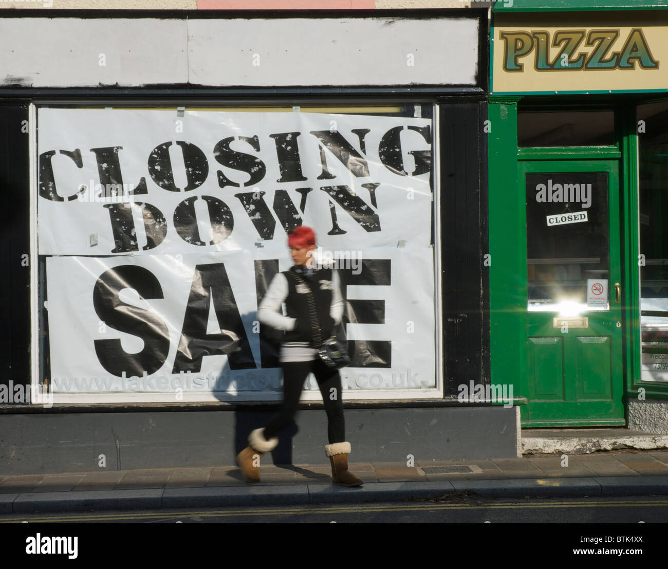 Young woman walking past 'Closing down sale' sign on shop window Stock
