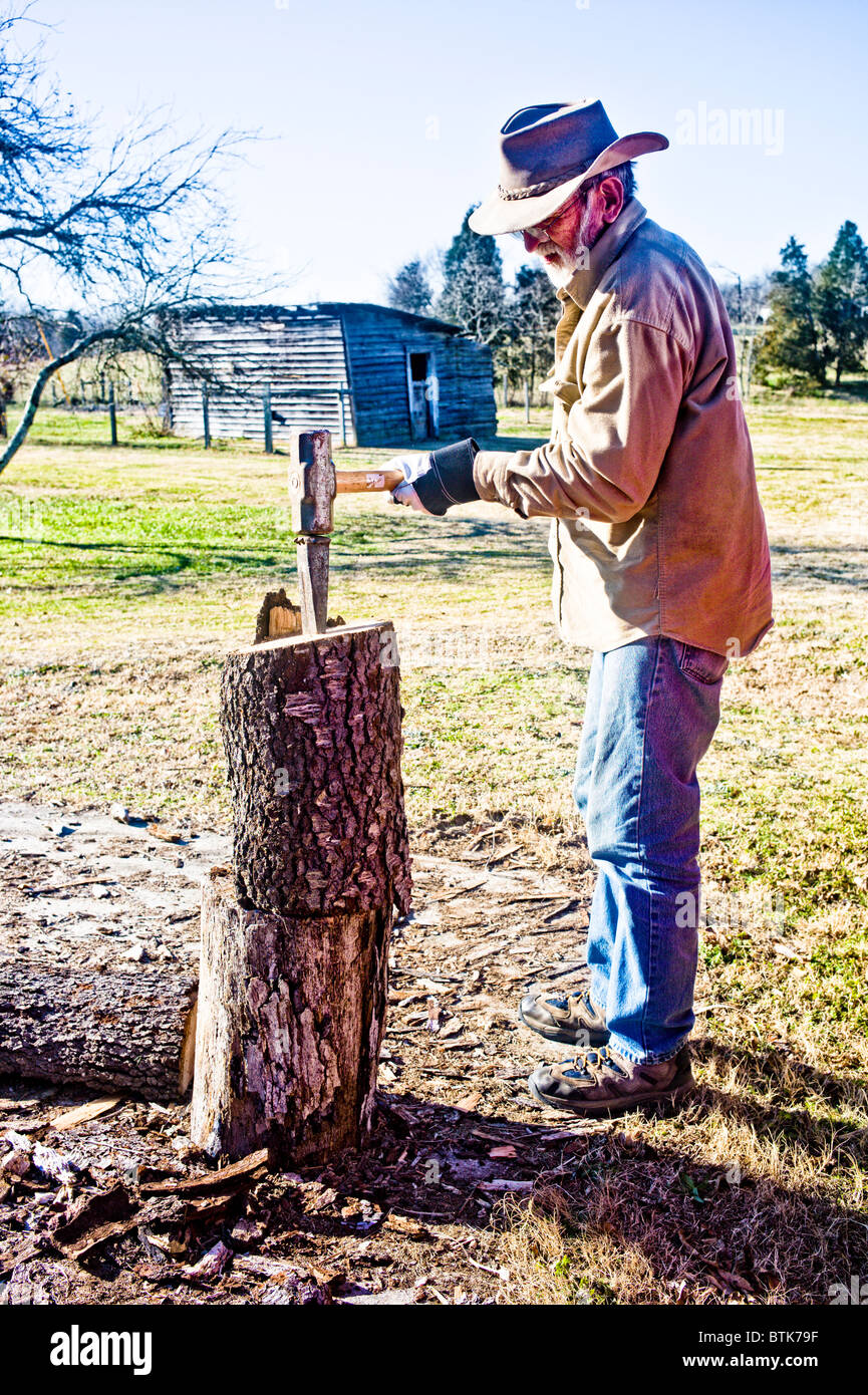 Farmer using a wedge and mallet to split hardwood logs for firewood on