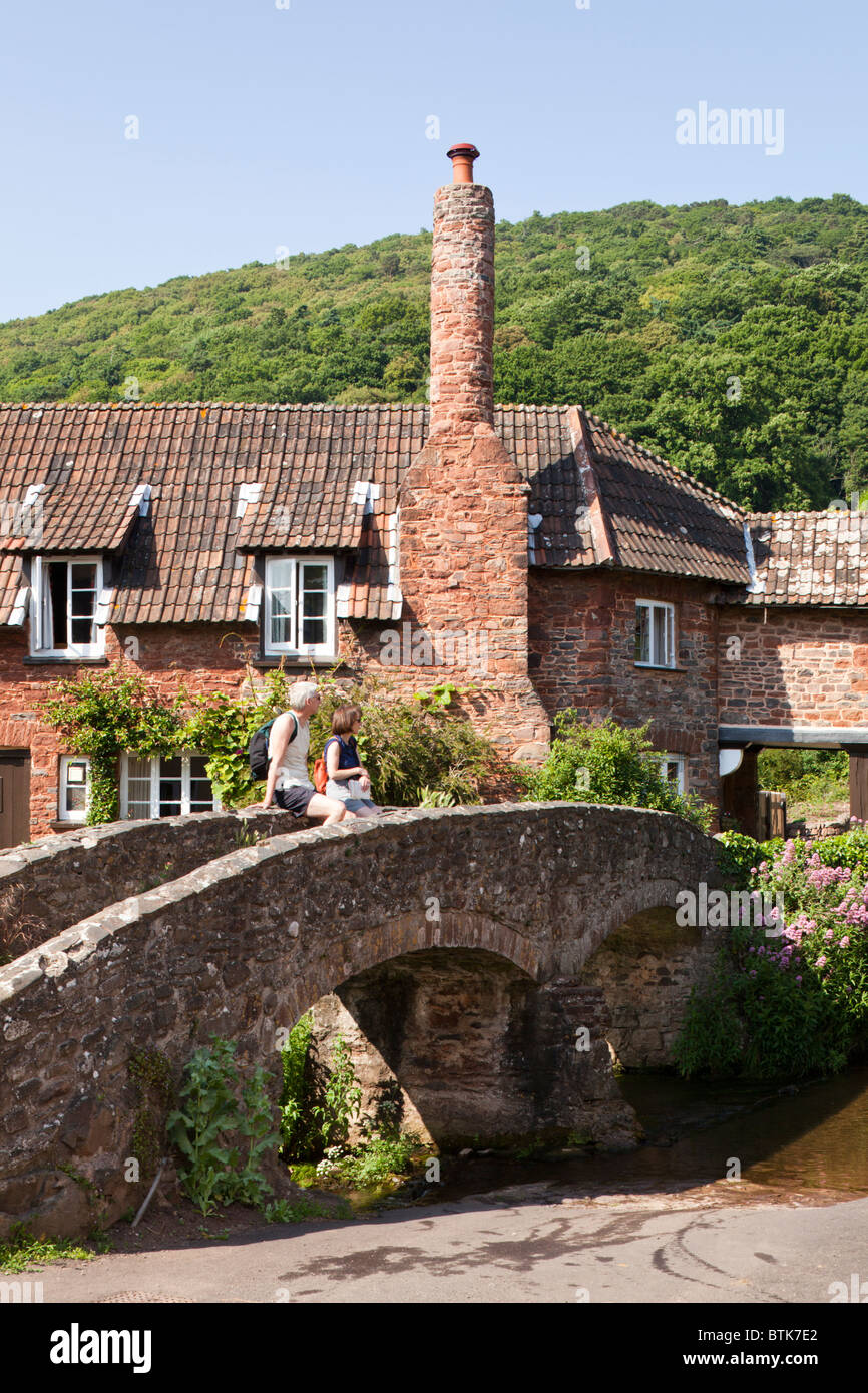 A couple of tourists enjoying the view from the ancient pack horse bridge over the River Aller at Allerford, Exmoor, Somerset Stock Photo