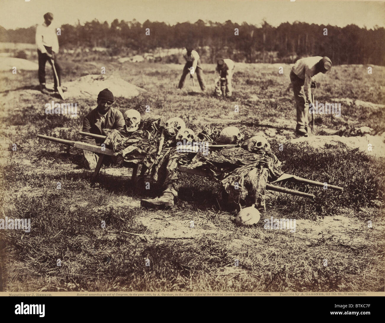 An African American soldier of a burial party on the battle-field of Cold Harbor seated next to a stretcher containing remains of Union soldiers who perished in the battles of Gaines' Mill and Cold Harbor. Assignment of a disproportionate number of African American soldiers to burial work continued in the 20th century. Stock Photo
