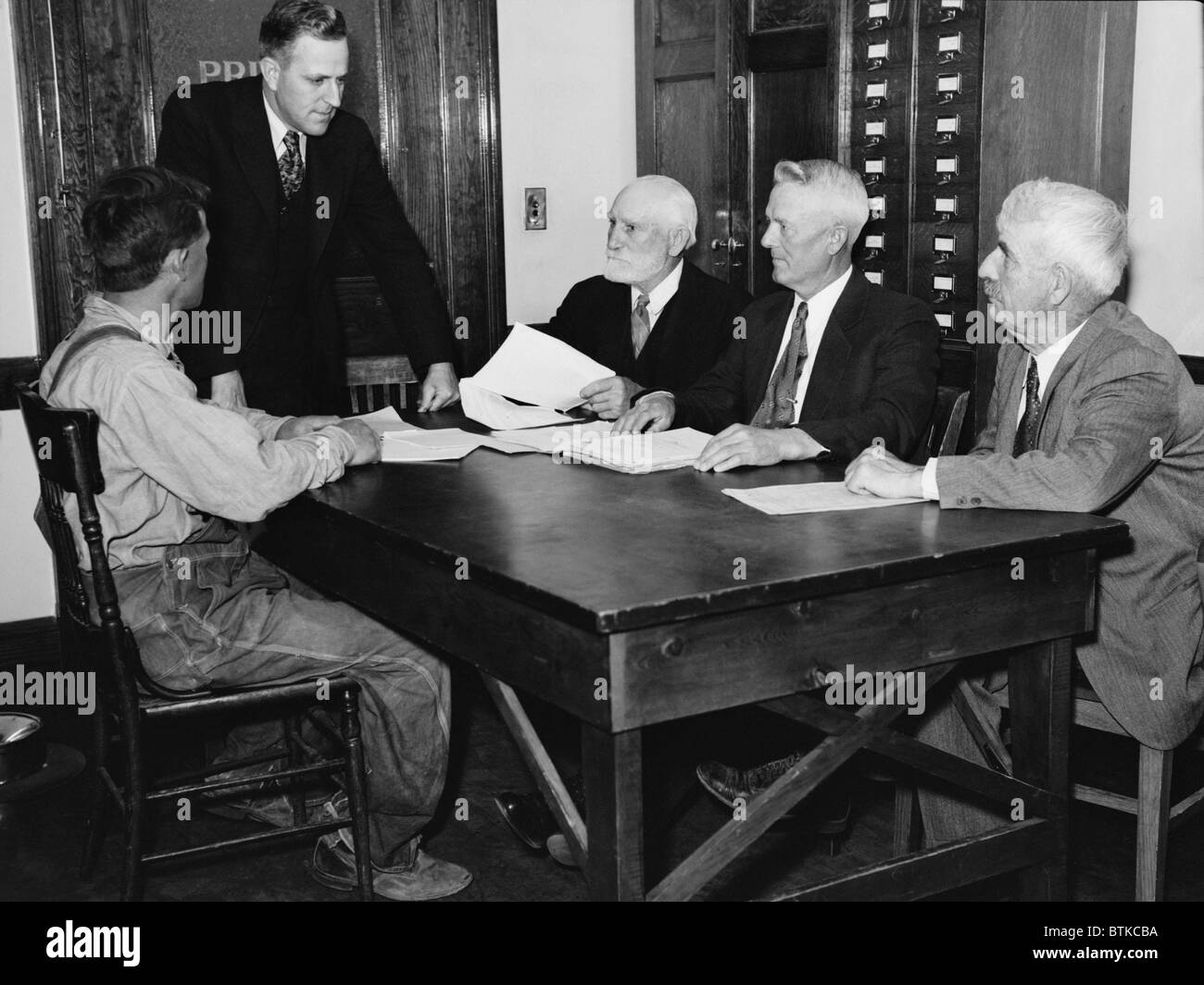 A Nebraska farmer meets with a Farm Security Administration Debt Adjustment Committee for help to avoiding foreclosure of his farm mortgage. The committee would negotiate with the bank to adjust his mortgage terms, allowing the farmer to remain in business. May 1936 photo by Arthur Rothstein. Stock Photo