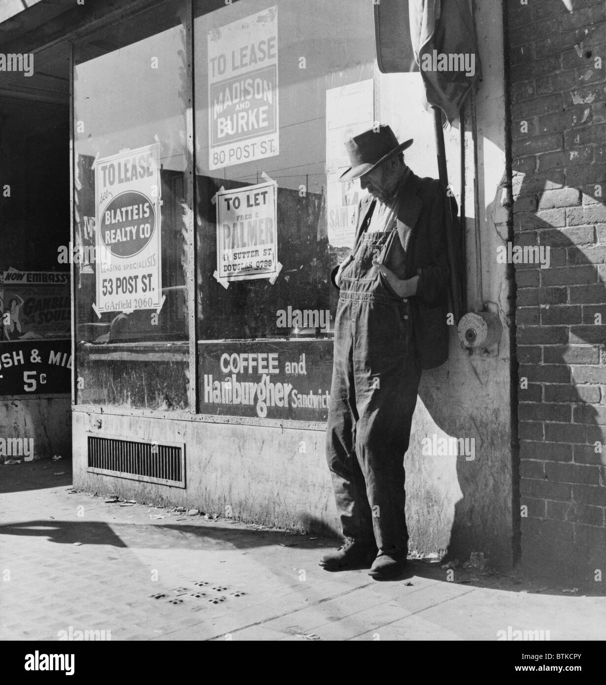 Lone man in farmer's overalls, on San Francisco's Skid Row at Howard Street. Ruined farmers from the Midwest added to the homeless and unemployed populations in California during the Great Depression. February 1936 photo by Dorothea Lange. Stock Photo