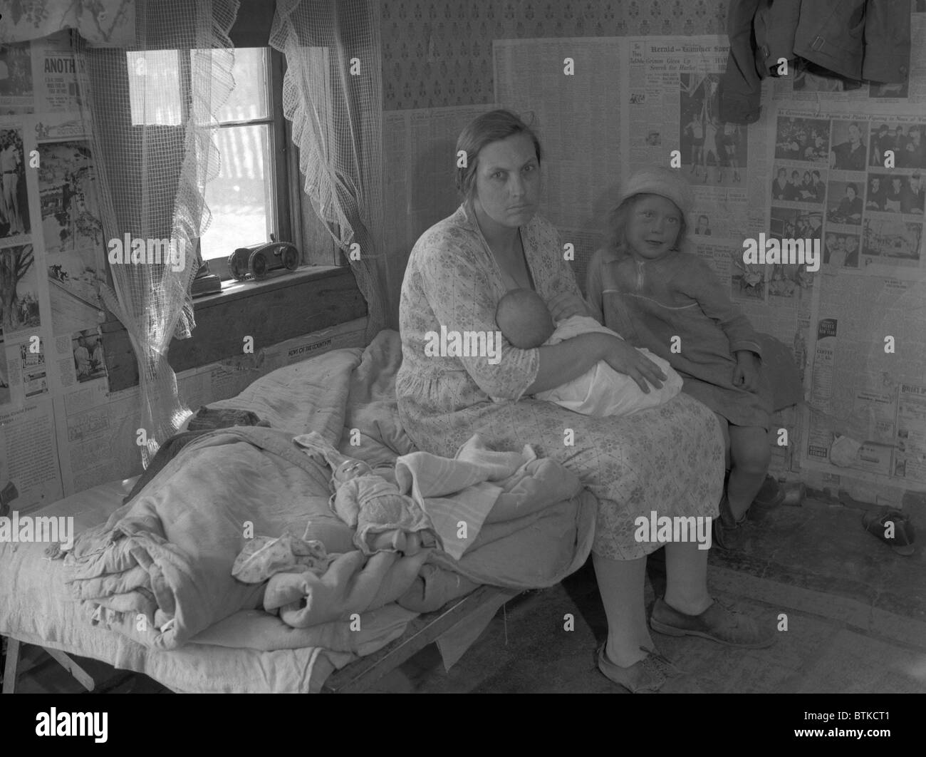Mother nursing her infant on a bed with another young child, surrounded ...