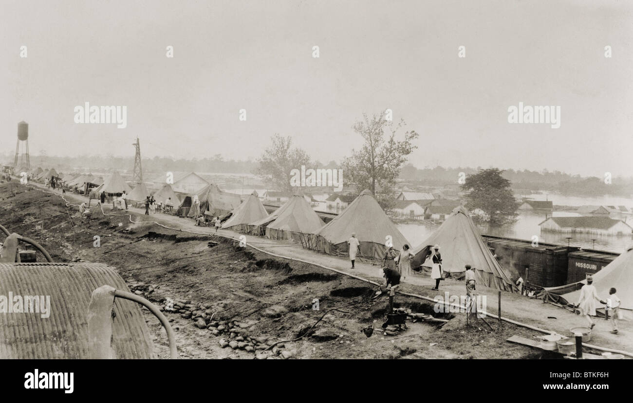 Refugees at a tent city on the levee, with partially submerged houses of Arkansas City in background, during the 1927 Flood. Stock Photo